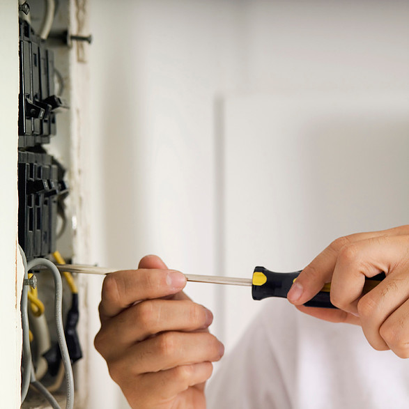 A man using a spanner to work on a wire on a wall